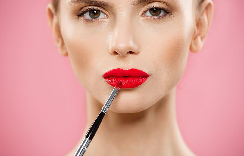 A woman applying bright red lipstick